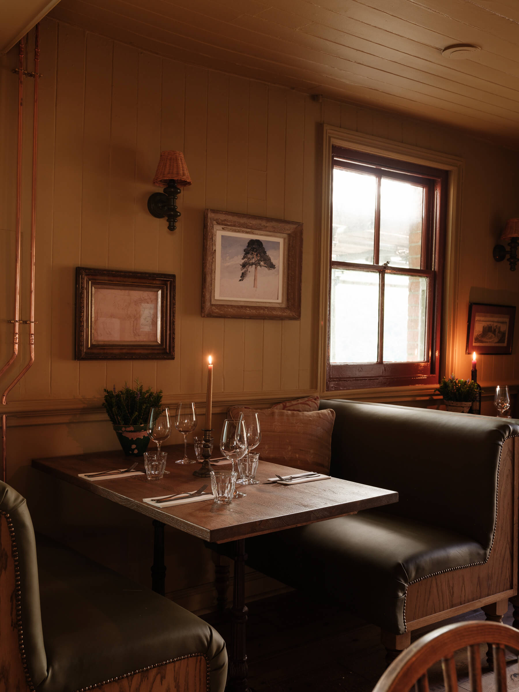 Pub interior, with paintings, wine glasses on a table, and leather long seats